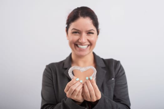 Caucasian woman holding two transparent heart-shaped aligners.