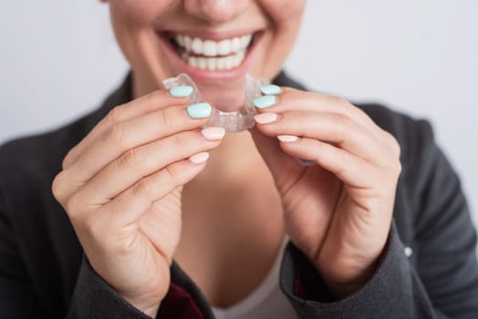 Close-up of a woman putting on transparent plastic retainers. The girl uses a device to straighten her teeth.