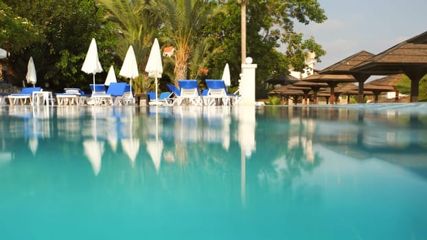 Empty sunbeds and closed parasols on morning, by the hotel pool. Photographed from water level. Vacation background, space for text down.