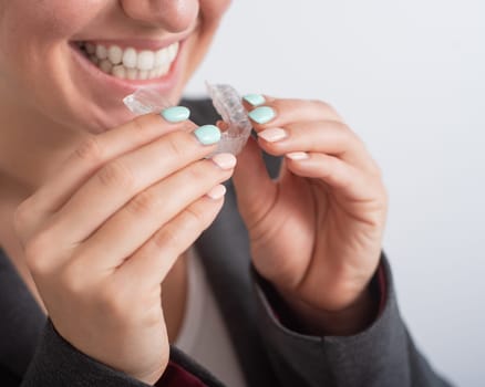 Close-up of a woman putting on transparent plastic retainers. The girl uses a device to straighten her teeth.