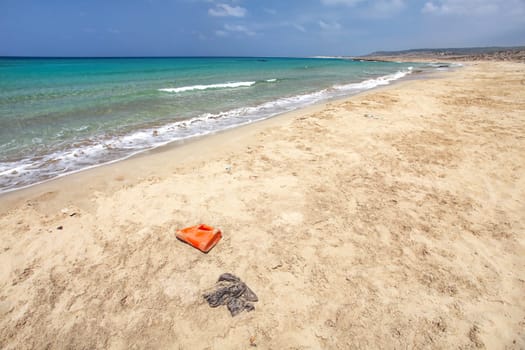 Beautiful wild beach with no tourists, crystal clear sea, but waste (plastic red bottle, black bag and other small debris) spoils the perfect picture. Ocean pollution concept.