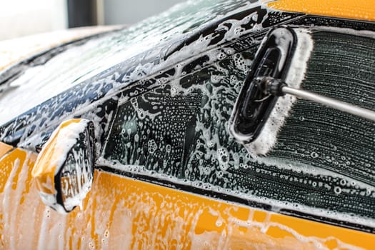 Yellow car side window washed in self service carwash. rush leaves strokes in shampoo and foam on glass.