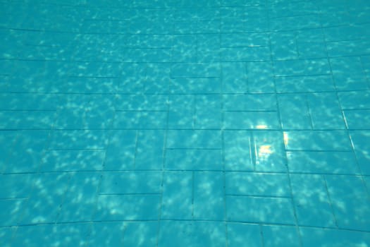 Swimming pool bottom, sun shining on blue tiles, lines distorted by water refraction.