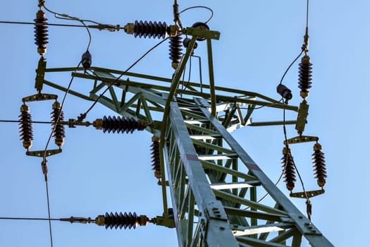 View from ground to power pylon top. Cables and ceramic isolators visible against blue sky. Abstract power industry background.