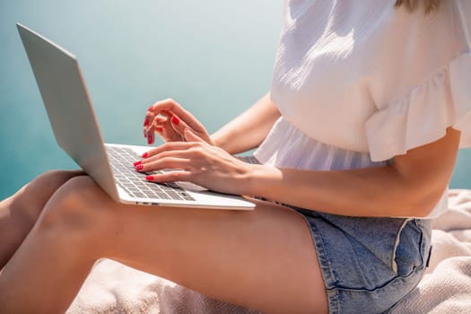 Freelance women sea working on the computer. Good looking middle aged woman typing on a laptop keyboard outdoors with a beautiful sea view. The concept of remote work