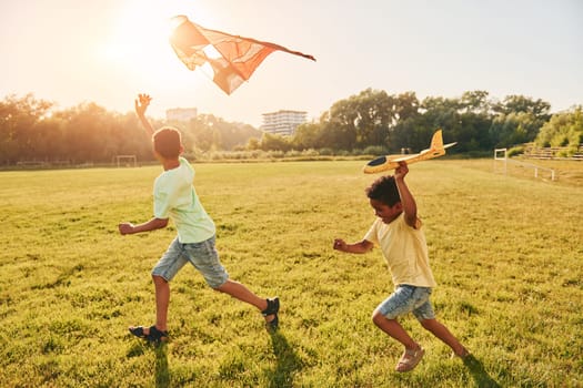 Running with kite. Two african american kids have fun in the field at summer daytime together.