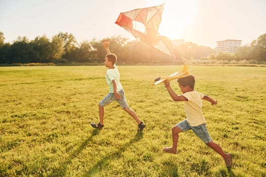 Running with kite. Two african american kids have fun in the field at summer daytime together.