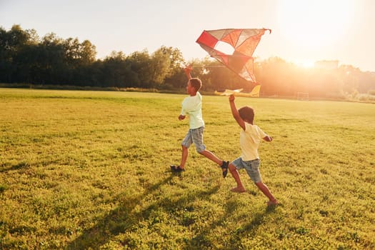 Running with kite. Two african american kids have fun in the field at summer daytime together.