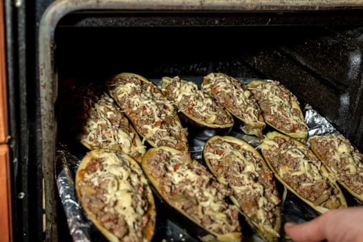 the hostess puts a baking tray with eggplant stuffed with meat in the oven. Eggplant halves stuffed with minced meat, spices and cheese, for baking in the oven. Delicious and healthy food