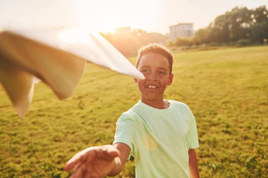 With paper plane. African american kid have fun in the field at summer daytime.