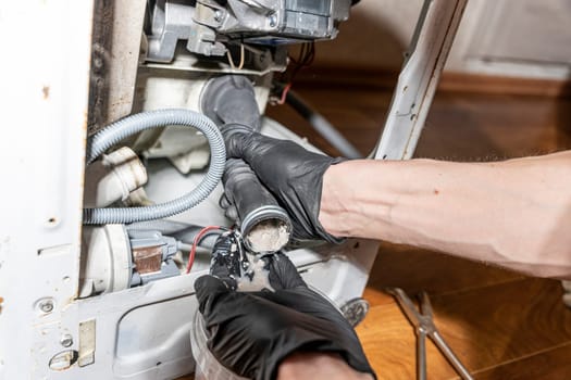 A repairman repairs a used washing machine. The water pump and rubber hoses are clogged with sediments. A jammed pump. calcium-magnesium deposits. Scum