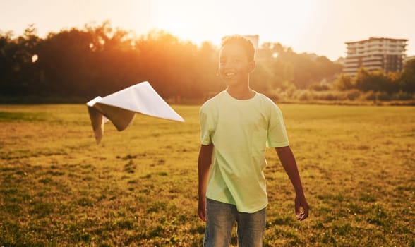 With paper plane. African american kid have fun in the field at summer daytime.