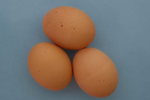 Top down view of three brown speckled chicken eggs on a blue background. High quality photo