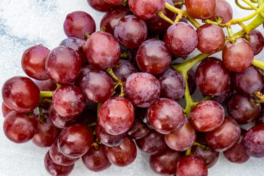 A bunch of juicy red grapes with stems on a white marble countertop. High quality photo