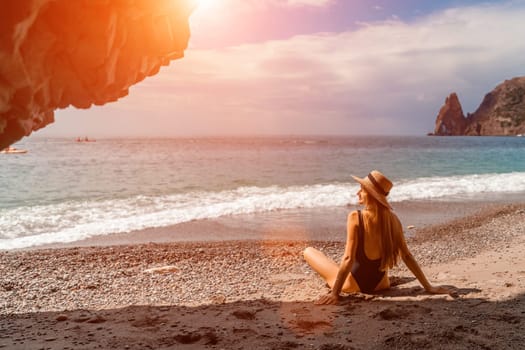 View of a woman in a black swimsuit from a sea cave Attractive woman enjoying the sea air sits on the beach and looks at the sea