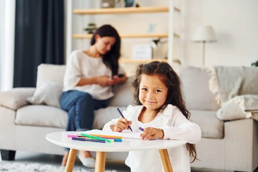 Girls is painting. Mother and her daughter spending time together at home.