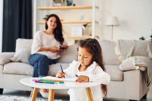 Girls is painting. Mother and her daughter spending time together at home.