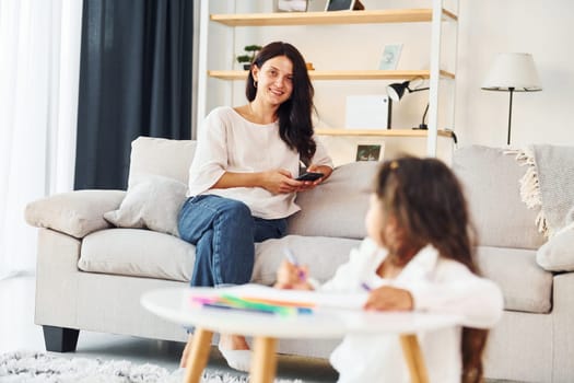 Girls is painting. Mother and her daughter spending time together at home.