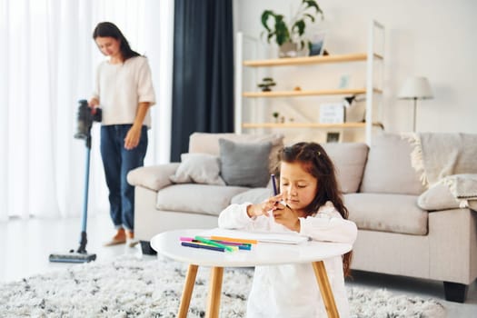 Girls is painting. Mother and her daughter spending time together at home.