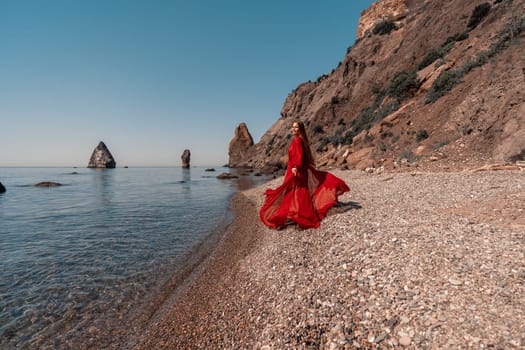 Happy woman in a flying red dress and with long hair, stands on the seashore.