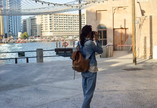 A young woman traveler with a backpack on her back walks and photographs the old narrow streets of Dubai Deira and Creek. Travel and sightseeing concept