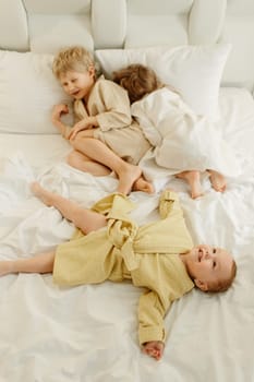 Children lie in a white bed in bathrobes after taking a bath, play and relax. view from above.