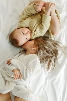 Girls sisters in bathrobes lie in bed. The older one kisses the younger one. View from above.