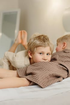 The boys lie on the bed in bathrobes after a shower. The elder put his head on the younger, looks into the camera.
