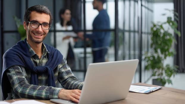 young businessman in glasses works with a computer remotely, sitting at the table.