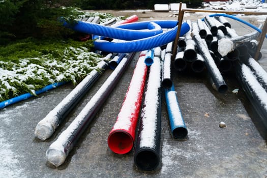 Blue, black and red pipelines of various diameters lie on a construction site outdoors in winter. Repair of communications.