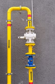 Yellow gas pipe with a shut-off - turn-on valve, connected to the wall of the building. Vertical frame.