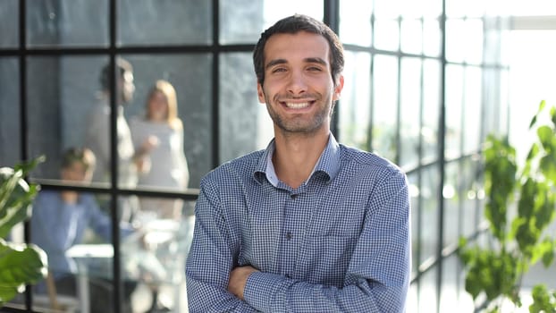 Young businessman in casual clothes stands with his hands on his waist in a modern office