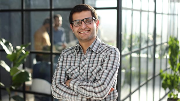 Young businessman with arms crossed standing in office lobby. success concept