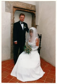 THE CZECHOSLOVAK REPUBLIC - CIRCA 1990s: Retro photo shows newlyweds. Bride wears long veil, white delicate wedding gown and bridal gloves. She holds a small bouquet of roses. Vintage color photography. Circa 1990.