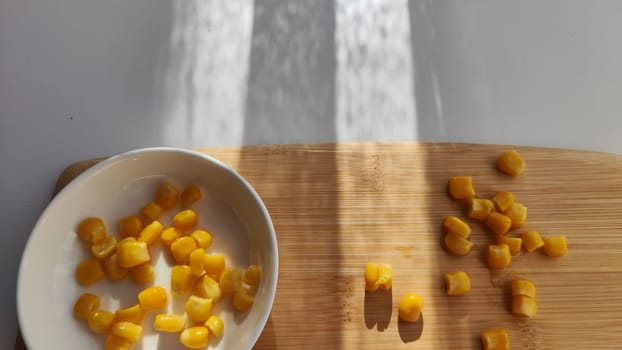 Lot of pieces of canned yellow corn on plate which is on wooden bamboo cutting board on white background. Concept of cooking and delicious healthy food