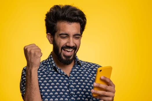 Happy excited joyful indian man in green shirt use smartphone typing browsing shouting say wow yes found out great big win, good news, lottery goal achievemen, celebrating success, winning game