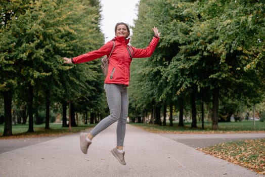 Young caucasian woman girl with toothy smile jumping in park forest outdoors looking at camera.