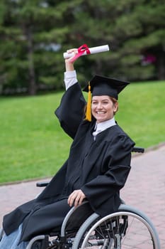 Caucasian woman in a wheelchair in a graduate costume rejoices at receiving a diploma