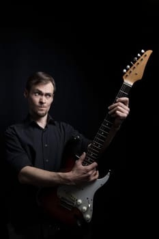 Young caucasian man learning to play electric guitar on black background.