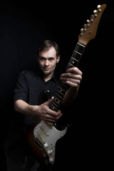 The guitarist picked up the guitar and pointed the neck towards the camera on black background.