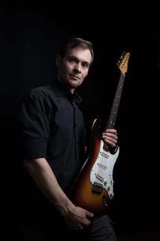 Studio low key portrait of caucasian man with electric guitar with dark lighting.