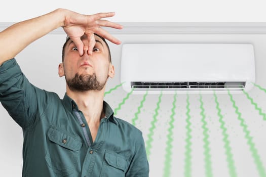 Man smells bad smell from dirty filter of split air conditionerin the room.