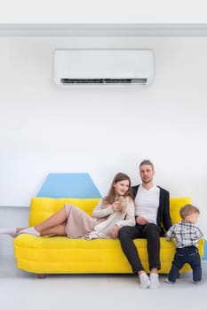 Young happy caucasian family lies on a yellow sofa in bright interior with split air conditioner.