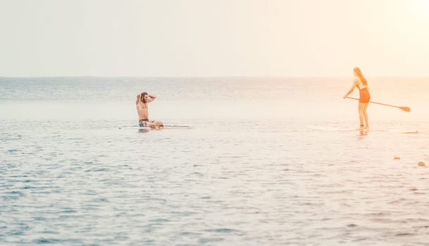 Sea woman and man on sup. Silhouette of happy young woman and man, surfing on SUP board, confident paddling through water surface. Idyllic sunset. Active lifestyle at sea or river