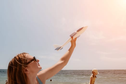 Woman hand holding toy airplane on blue sky and white clouds at seaside, dream of travel by plane. Happy woman has fun in summer vacation by sea and mountains. Lifestyle moment