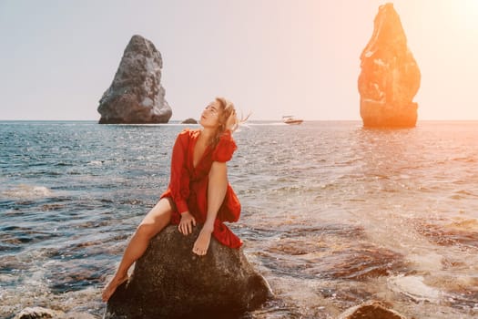 Woman travel sea. Young Happy woman in a long red dress posing on a beach near the sea on background of volcanic rocks, like in Iceland, sharing travel adventure journey