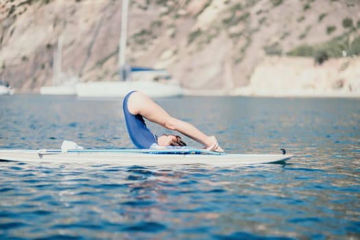 Woman sup yoga. Middle age sporty woman practising yoga pilates on paddle sup surfboard. Female stretching doing workout on sea water. Modern individual hipster outdoor summer sport activity