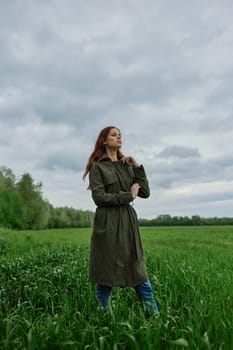 a beautiful woman in a dark coat stands in a green field in the spring in rainy weather. High quality photo