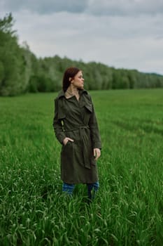 a beautiful woman in a dark coat stands in a green field in the spring in rainy weather. High quality photo