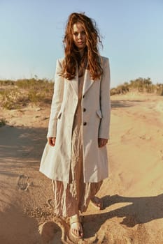 a red-haired woman stands in the desert in light clothes in windy weather looking at the camera. High quality photo